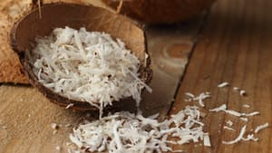 Photo showing an opened coconut shell with shredded coconut inside