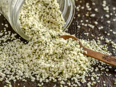 Photo of glass jar on its side spilling hemp seeds over wooden table