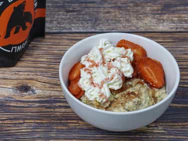 Growli Muesli bowl with sliced strawberries, spray cream and strawberry syrup drizzled over